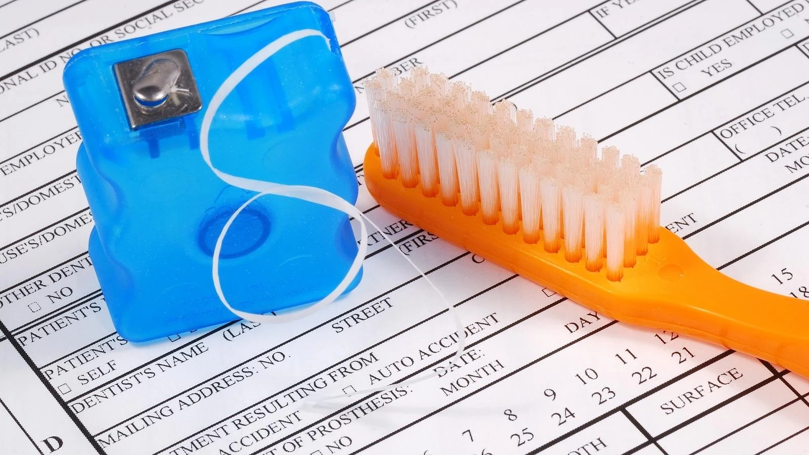 Hilo dental y cepillo de dientes naranja sobre formularios de un paciente
