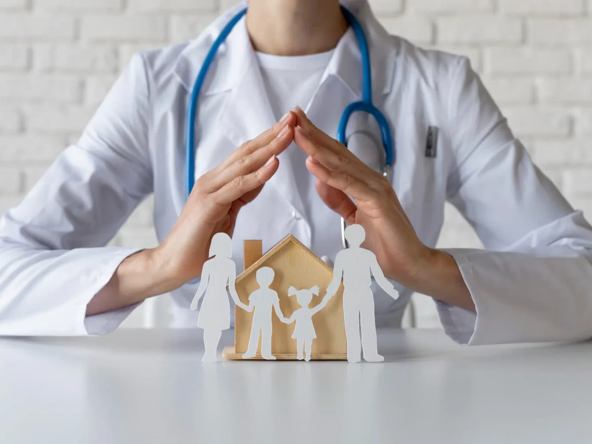 Médico protegiendo con ambas manos unas figuras de madera que representan a una familia