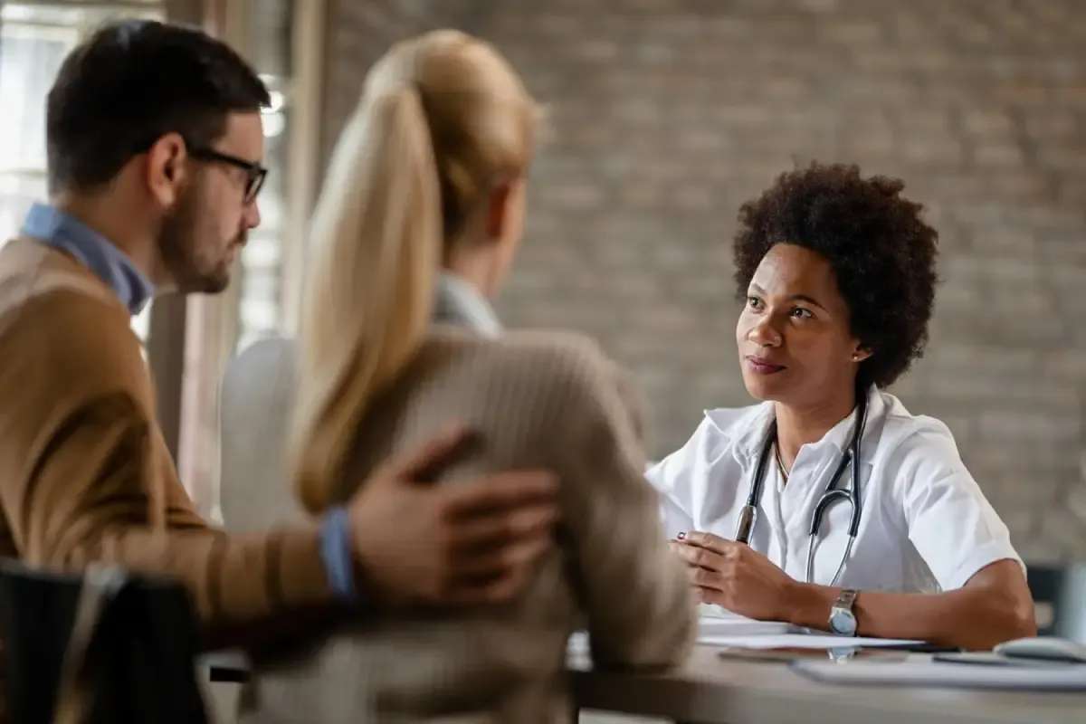Pareja que consulta con una doctora atenta en un escritorio.